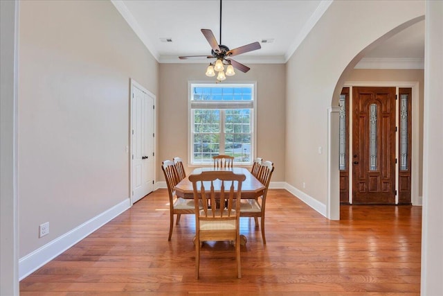 dining area with ornamental molding, arched walkways, a ceiling fan, and light wood-style flooring
