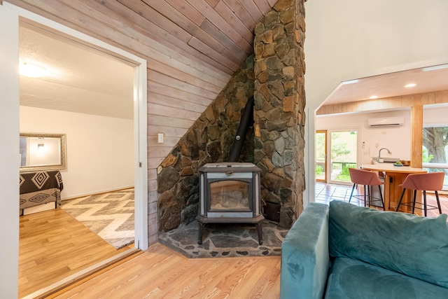 living area with a wood stove, an AC wall unit, lofted ceiling, and wood finished floors