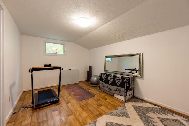 workout area featuring baseboards, wood finished floors, a textured ceiling, and vaulted ceiling