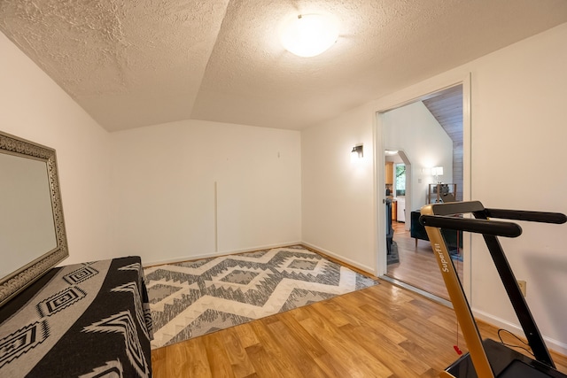 workout area with a textured ceiling, arched walkways, lofted ceiling, and wood finished floors