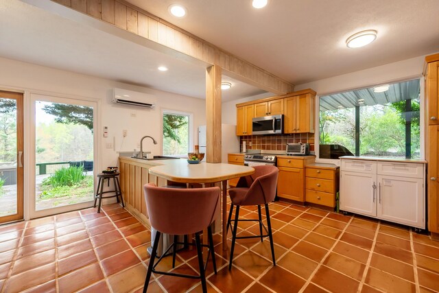 kitchen with appliances with stainless steel finishes, an AC wall unit, backsplash, a sink, and a peninsula
