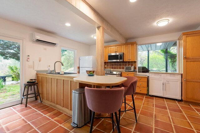 kitchen with a sink, a wall mounted AC, stainless steel appliances, tasteful backsplash, and a peninsula