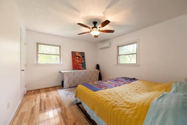 bedroom with baseboards, multiple windows, a wall unit AC, and light wood-type flooring