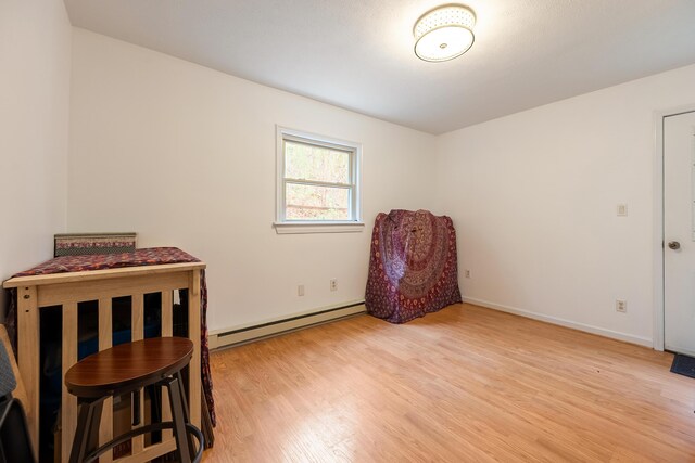 living area with a baseboard heating unit, light wood-style flooring, and baseboards