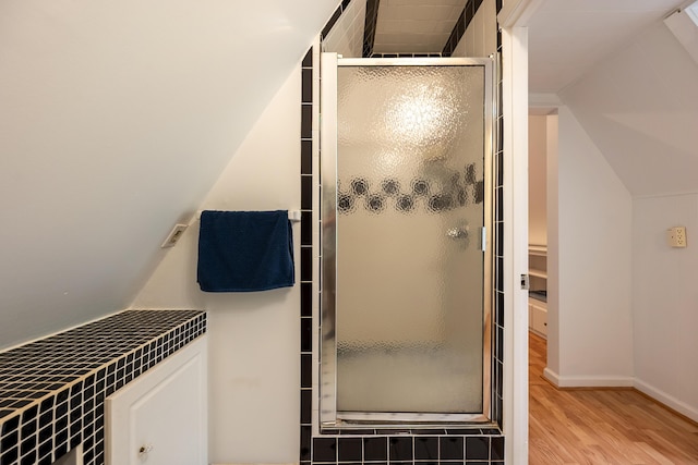 full bathroom with wood finished floors, a shower stall, vaulted ceiling, baseboards, and a spacious closet