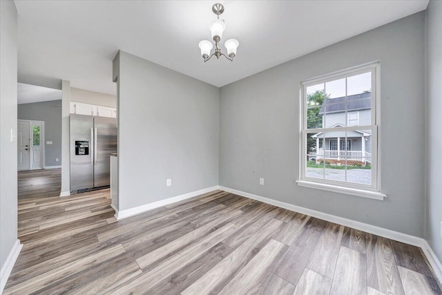 unfurnished dining area featuring light wood-type flooring, baseboards, and a notable chandelier