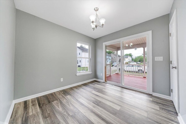 unfurnished dining area featuring baseboards, a notable chandelier, and wood finished floors