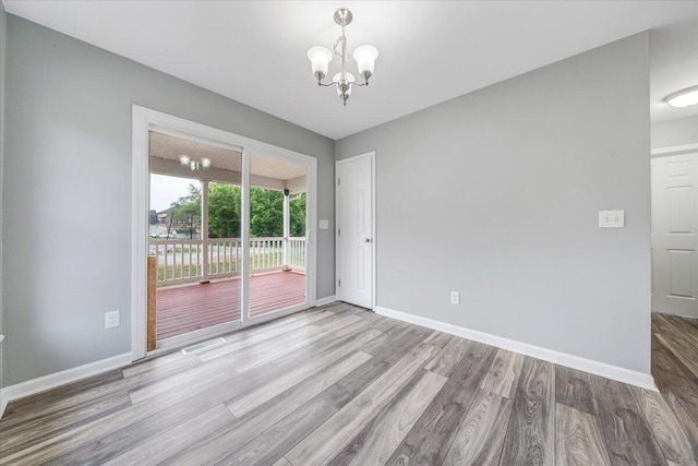 empty room with baseboards, wood finished floors, a chandelier, and visible vents