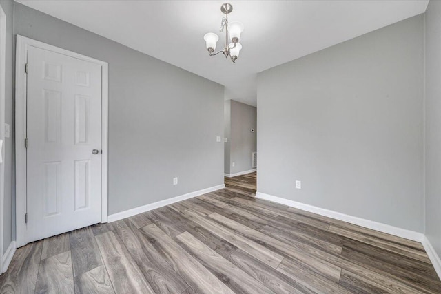 empty room with an inviting chandelier, baseboards, and wood finished floors