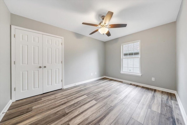 unfurnished bedroom featuring baseboards, wood finished floors, and a closet