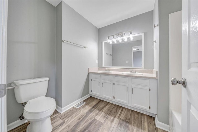 full bath with a sink, double vanity, toilet, and wood finished floors