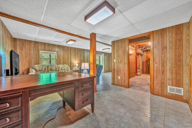 office area with a paneled ceiling, visible vents, and wood walls