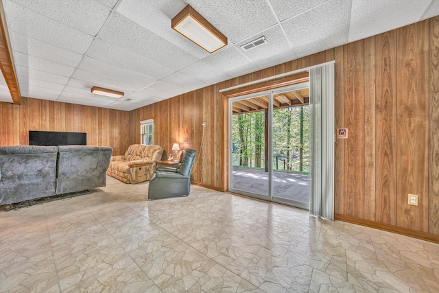 living area with wood walls, a drop ceiling, visible vents, and baseboards