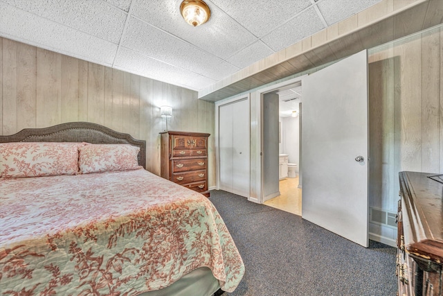 bedroom with carpet flooring, wood walls, and ensuite bathroom