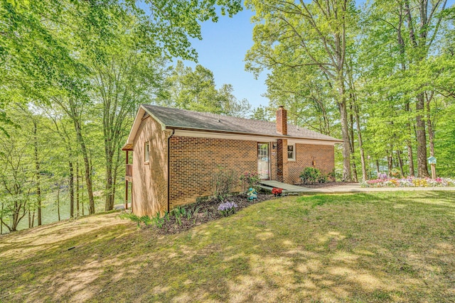 view of side of home with brick siding, a yard, and a chimney