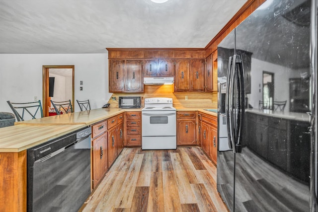 kitchen featuring under cabinet range hood, black appliances, light wood-type flooring, a peninsula, and brown cabinetry