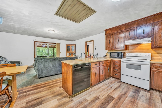 kitchen featuring light wood-style flooring, under cabinet range hood, light countertops, black appliances, and a peninsula