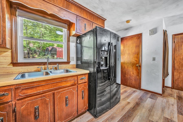 kitchen with brown cabinetry, light countertops, black fridge, and a sink
