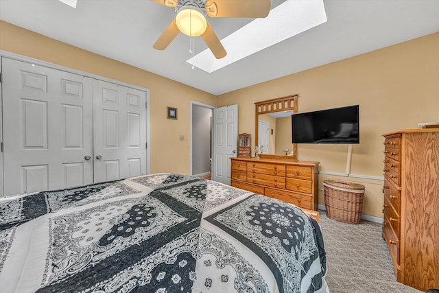 carpeted bedroom featuring a skylight, baseboards, a ceiling fan, and a closet