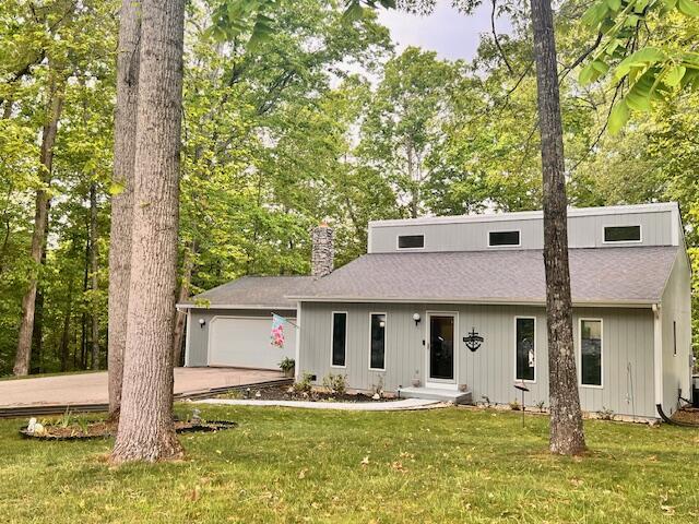 view of front of house featuring an attached garage, driveway, a chimney, and a front lawn