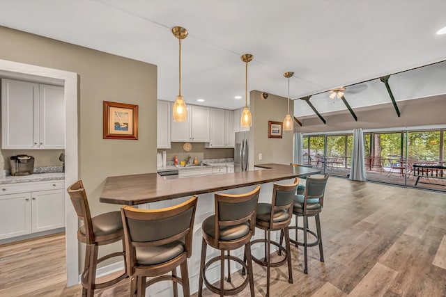 kitchen with a breakfast bar, a sink, freestanding refrigerator, white cabinetry, and light wood-type flooring