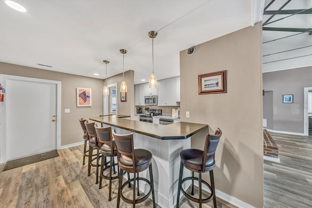 kitchen with wood finished floors, baseboards, white cabinets, a breakfast bar, and stainless steel appliances