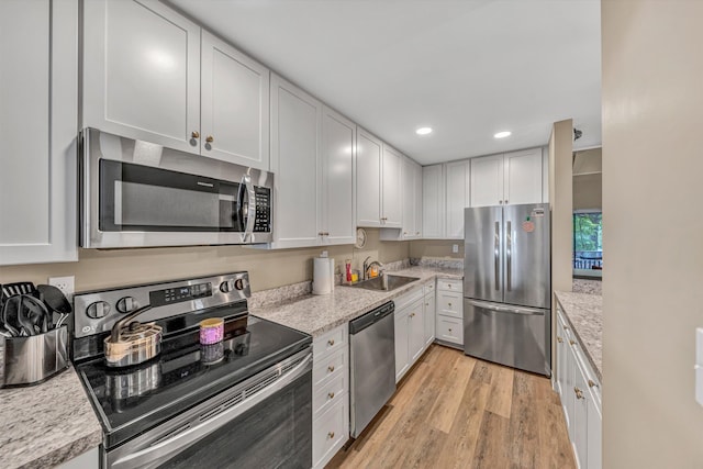 kitchen featuring white cabinets, a sink, light wood finished floors, stainless steel appliances, and recessed lighting