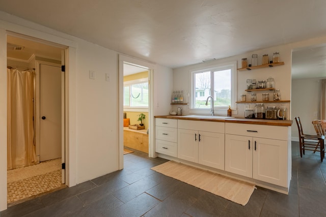 kitchen with butcher block countertops, open shelves, a sink, white cabinetry, and visible vents
