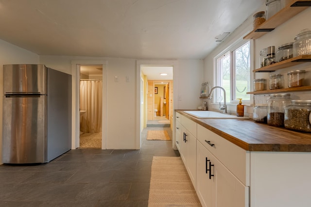 kitchen featuring butcher block counters, freestanding refrigerator, open shelves, a sink, and white cabinetry