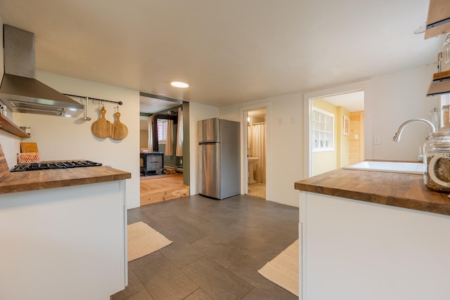 kitchen with a sink, wall chimney exhaust hood, butcher block countertops, and freestanding refrigerator