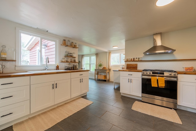kitchen featuring a sink, stainless steel gas range oven, open shelves, and wall chimney range hood