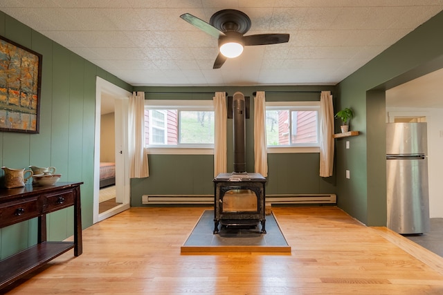 exercise area with a wood stove, wood finished floors, a baseboard heating unit, and ceiling fan