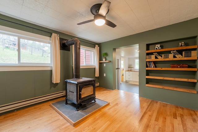 interior space featuring a baseboard heating unit, a wood stove, a ceiling fan, and wood finished floors