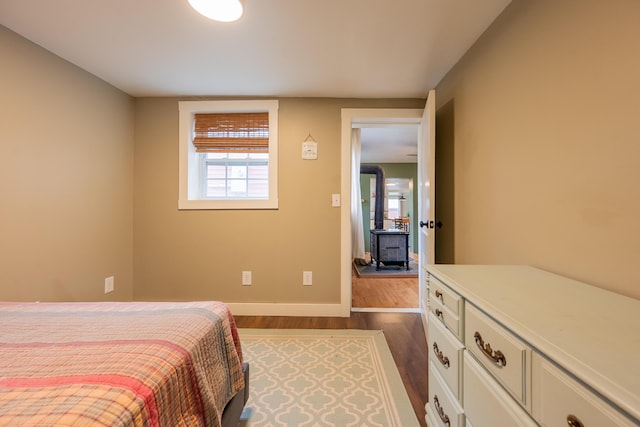 bedroom with a wood stove, dark wood finished floors, and baseboards