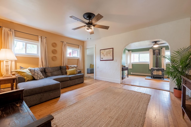 living area featuring a wood stove, a ceiling fan, arched walkways, and light wood finished floors