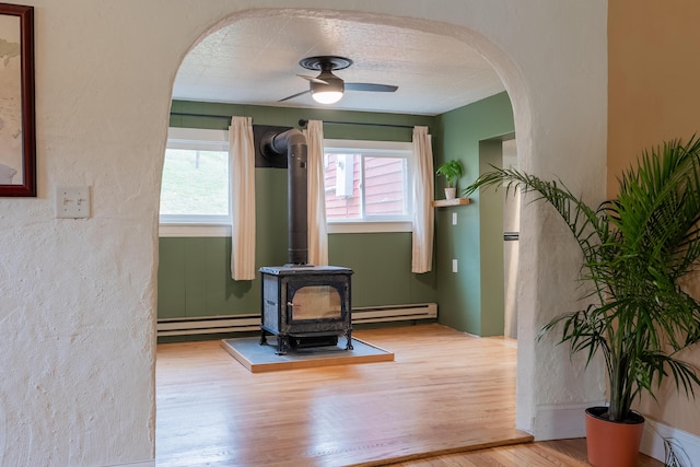 interior details featuring wood finished floors, arched walkways, a baseboard radiator, ceiling fan, and a wood stove
