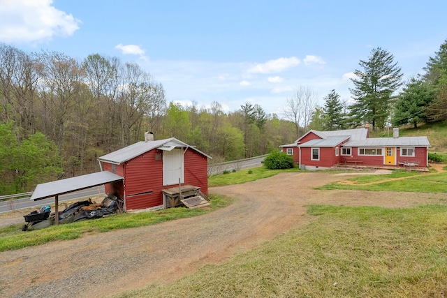 view of outbuilding with an outdoor structure, dirt driveway, a view of trees, and fence