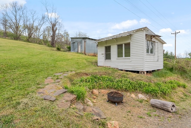 view of home's exterior with an outdoor structure, a lawn, and a fire pit