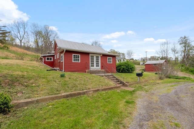 view of front of home with metal roof, dirt driveway, entry steps, french doors, and a front yard