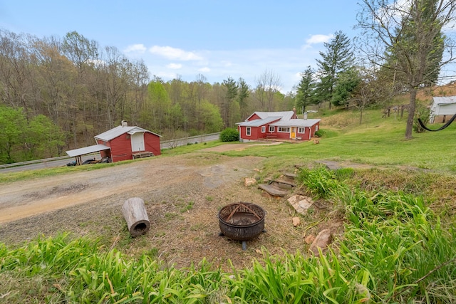 view of yard with an outdoor structure, a forest view, driveway, a fire pit, and fence