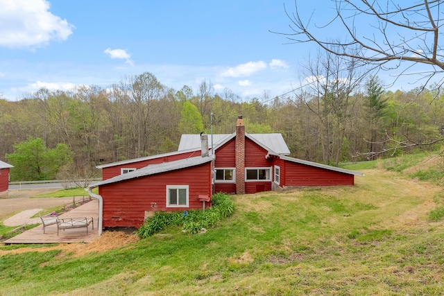 rear view of property featuring a lawn, a chimney, a deck, and a forest view