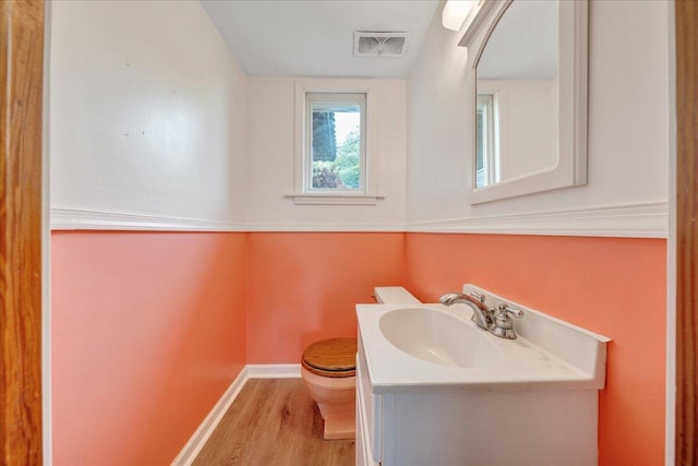 half bathroom featuring visible vents, wood finished floors, vanity, baseboards, and toilet