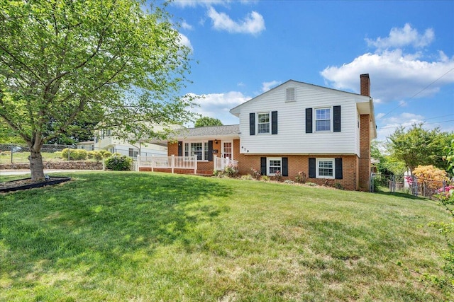 split level home featuring brick siding, fence, a chimney, and a front yard
