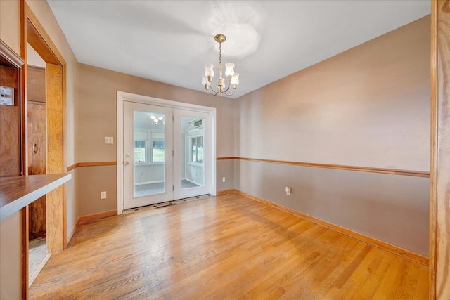 empty room with an inviting chandelier, baseboards, french doors, and light wood-style flooring