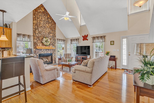 living area featuring a ceiling fan, a stone fireplace, high vaulted ceiling, baseboards, and light wood-style flooring