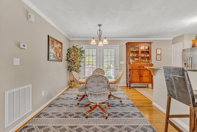dining room featuring visible vents, ornamental molding, light wood-style floors, baseboards, and a chandelier