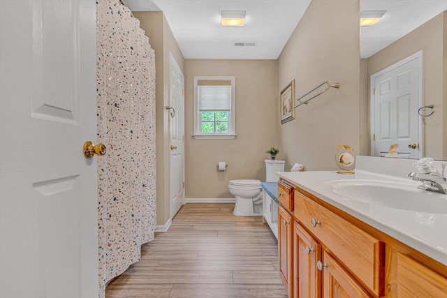 bathroom with visible vents, vanity, wood finished floors, toilet, and baseboards