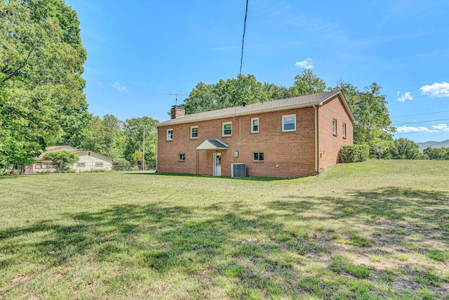 back of property with a lawn, brick siding, central air condition unit, and a chimney