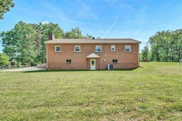 rear view of property with a yard, brick siding, a chimney, and central AC unit