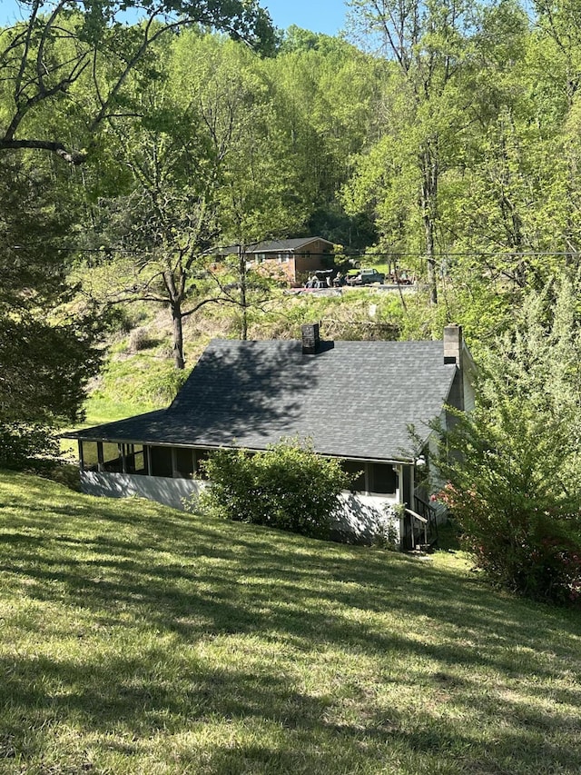 view of property exterior featuring a lawn, a chimney, a shingled roof, and a view of trees